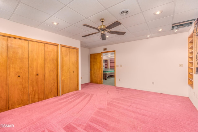 unfurnished bedroom with two closets, a paneled ceiling, ceiling fan, and carpet flooring