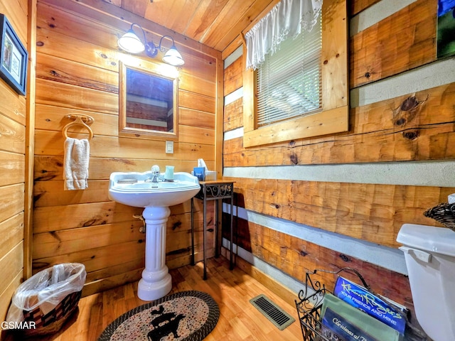 bathroom with wooden walls, toilet, wooden ceiling, wood finished floors, and visible vents