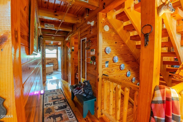 hallway featuring wood finished floors, wood ceiling, beamed ceiling, and wood walls