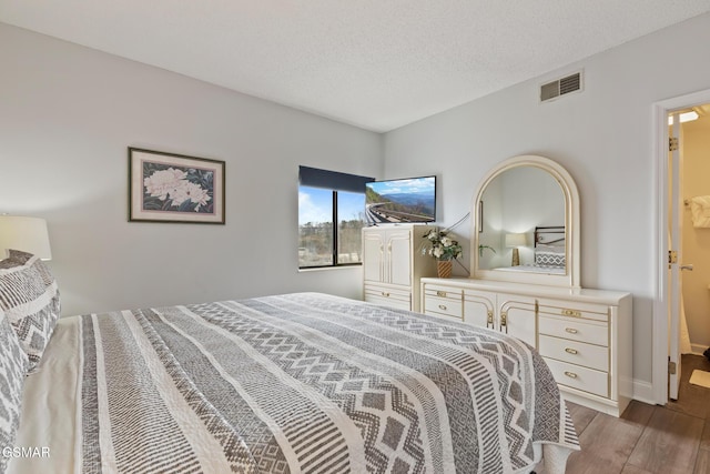 bedroom with a textured ceiling, light wood-style flooring, visible vents, and baseboards