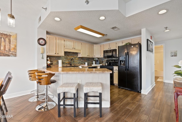 kitchen with a peninsula, dark wood-style flooring, a sink, backsplash, and black appliances