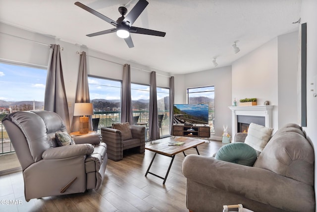 living room with a ceiling fan, a lit fireplace, and wood finished floors