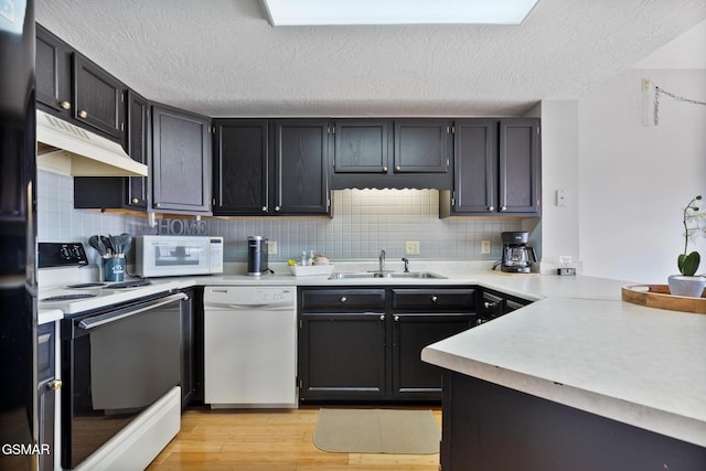 kitchen featuring white appliances, light wood finished floors, light countertops, under cabinet range hood, and a sink