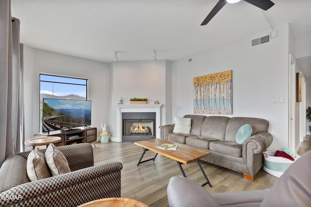 living area with a lit fireplace, visible vents, ceiling fan, and wood finished floors