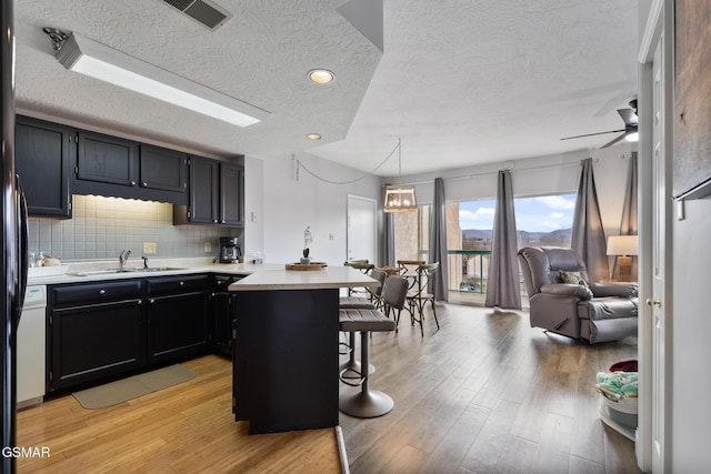 kitchen featuring a breakfast bar area, a peninsula, a sink, open floor plan, and light countertops