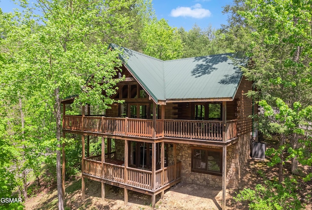 back of house with a deck, log siding, metal roof, and stone siding