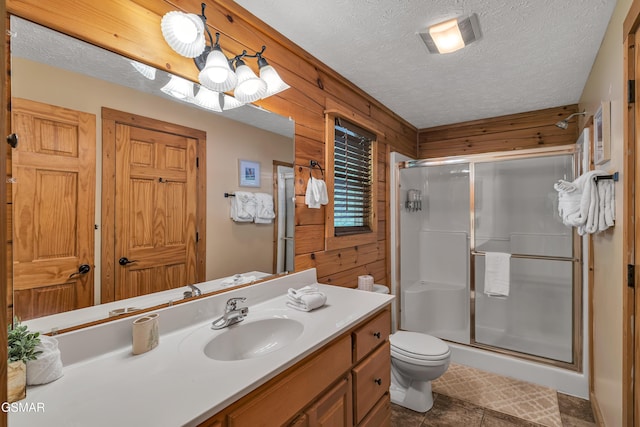 bathroom featuring vanity, toilet, wooden walls, a textured ceiling, and a stall shower