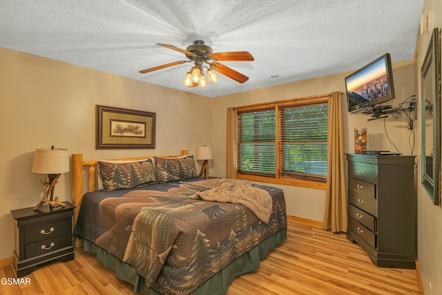 bedroom with light wood-type flooring, a textured ceiling, baseboards, and ceiling fan