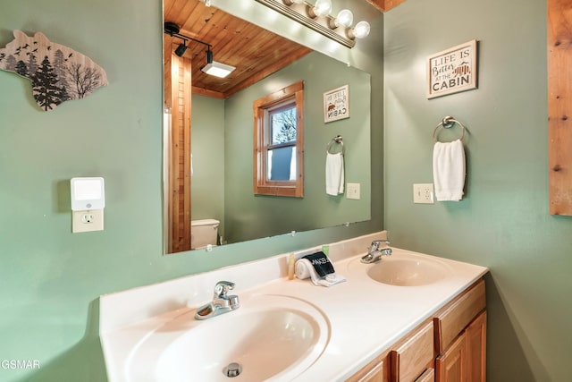 bathroom with toilet, wood ceiling, double vanity, and a sink