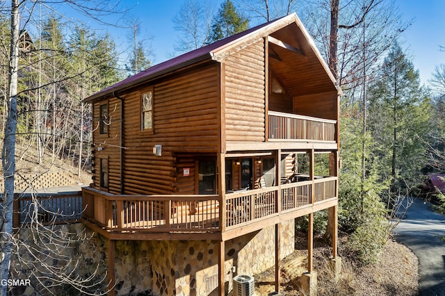 back of property featuring stone siding, cooling unit, a wooden deck, and a balcony