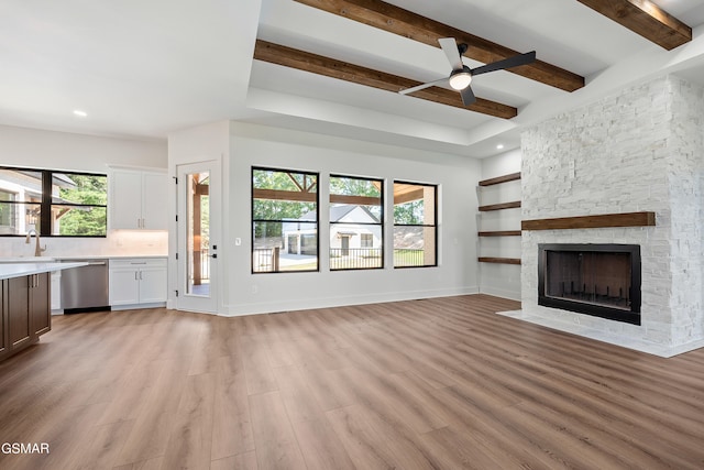 unfurnished living room with light hardwood / wood-style floors, a stone fireplace, ceiling fan, and a healthy amount of sunlight