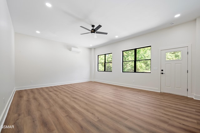 interior space with light hardwood / wood-style flooring, an AC wall unit, and ceiling fan