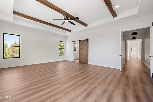 spare room featuring a tray ceiling, a barn door, ceiling fan, and light hardwood / wood-style flooring