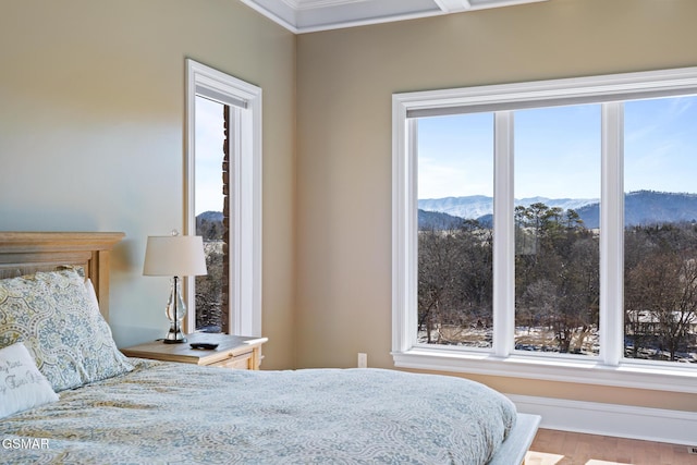 bedroom with a mountain view, multiple windows, wood finished floors, and ornamental molding