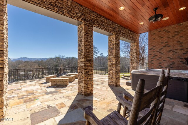 view of patio / terrace featuring fence, a forest view, and a hot tub