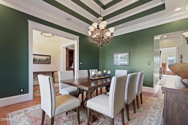 dining room featuring a raised ceiling, a notable chandelier, crown molding, and light wood finished floors