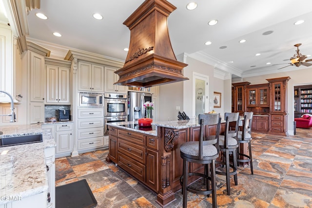 kitchen featuring stone tile floors, island exhaust hood, a sink, appliances with stainless steel finishes, and cream cabinets