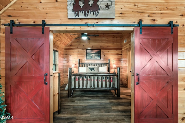 bedroom with hardwood / wood-style floors, wood walls, a barn door, and vaulted ceiling