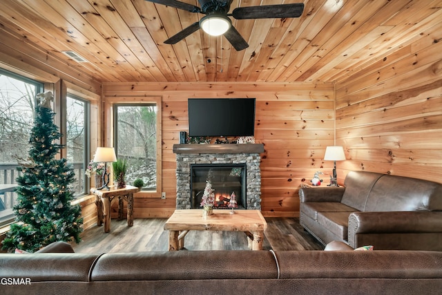 living room with hardwood / wood-style floors, wood ceiling, a stone fireplace, wooden walls, and ceiling fan