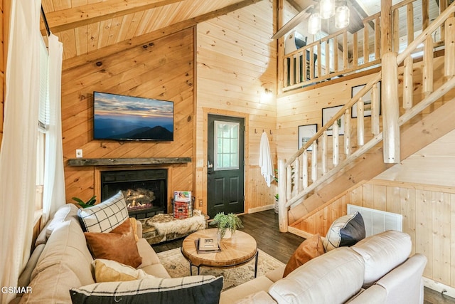 living room featuring stairway, wooden walls, wood finished floors, a warm lit fireplace, and wood ceiling