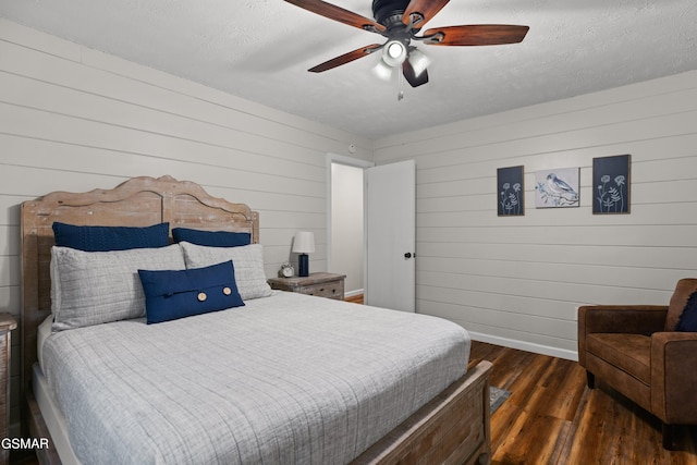 bedroom with a textured ceiling, ceiling fan, dark wood-type flooring, and wood walls