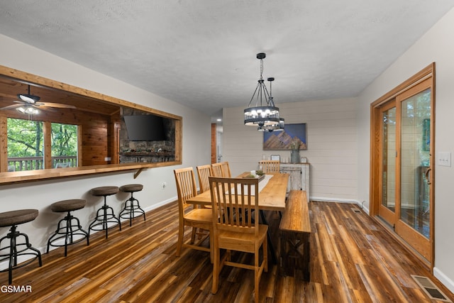 dining space featuring ceiling fan with notable chandelier, a textured ceiling, dark hardwood / wood-style floors, and wood walls