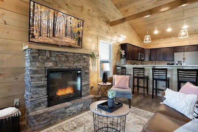 living room with wood walls, light hardwood / wood-style flooring, vaulted ceiling with beams, a fireplace, and wood ceiling