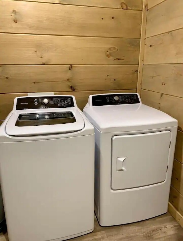 washroom with washer and dryer, light hardwood / wood-style flooring, and wooden walls