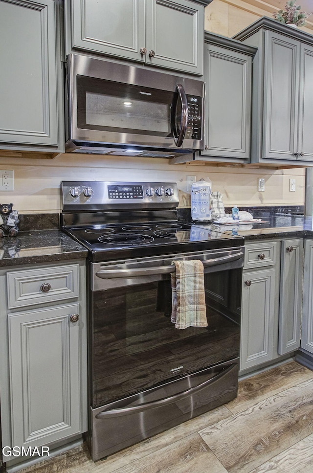 kitchen featuring black range with electric cooktop, gray cabinets, light hardwood / wood-style flooring, and dark stone countertops