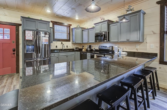 kitchen with wooden ceiling, stainless steel appliances, dark stone countertops, pendant lighting, and wooden walls