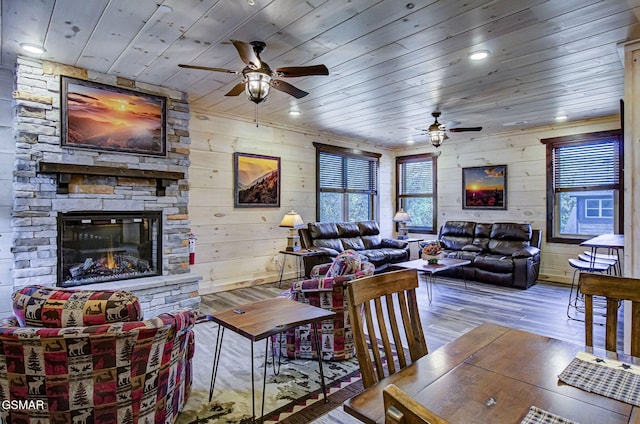 living room with wooden ceiling, a stone fireplace, wooden walls, ceiling fan, and light hardwood / wood-style floors