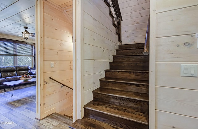 stairs with hardwood / wood-style flooring, ceiling fan, and wooden walls