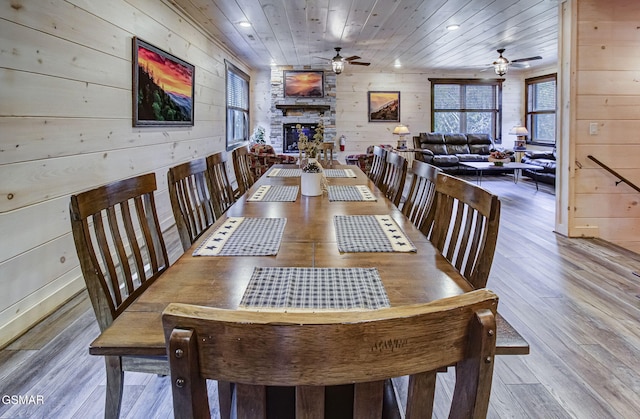 dining space with hardwood / wood-style floors, wooden ceiling, a fireplace, and wooden walls