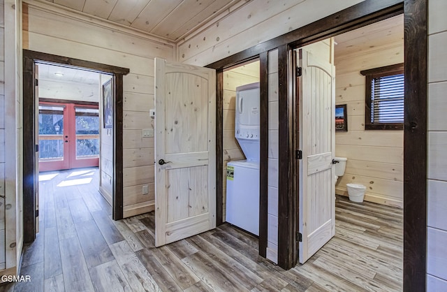 hall with light wood-type flooring, stacked washing maching and dryer, wooden walls, and french doors