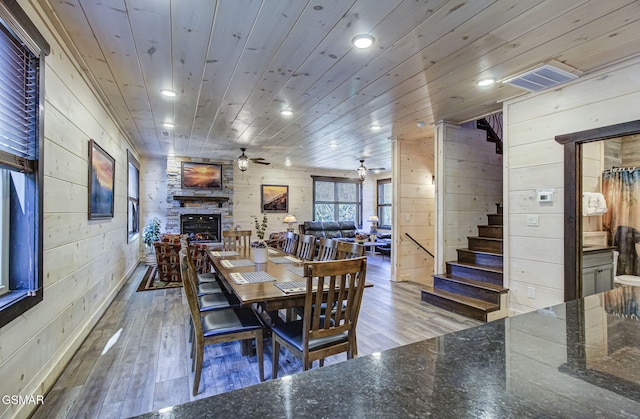 dining area featuring ceiling fan, wooden ceiling, a stone fireplace, wood walls, and light hardwood / wood-style floors