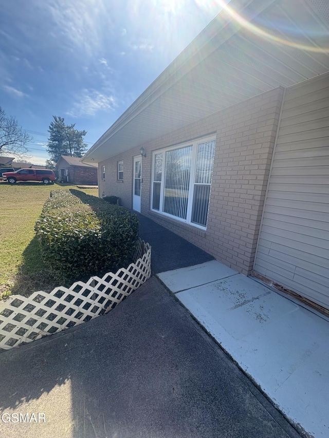 view of side of property with a patio, brick siding, and a lawn