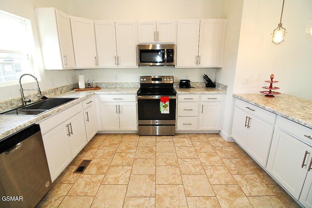 kitchen featuring light stone countertops, appliances with stainless steel finishes, sink, white cabinetry, and hanging light fixtures