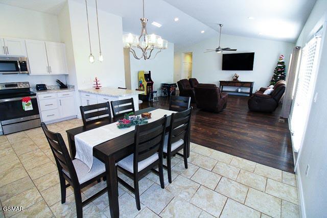 tiled dining room with lofted ceiling and ceiling fan with notable chandelier