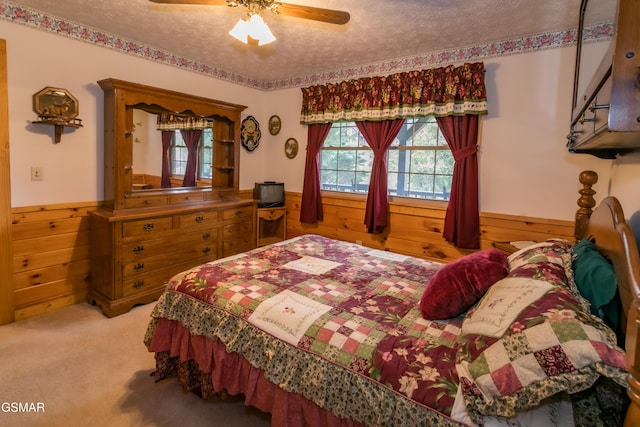 bedroom featuring carpet, a textured ceiling, ceiling fan, and wooden walls