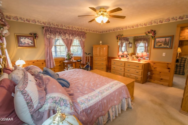 bedroom with light colored carpet, ceiling fan, and wooden walls