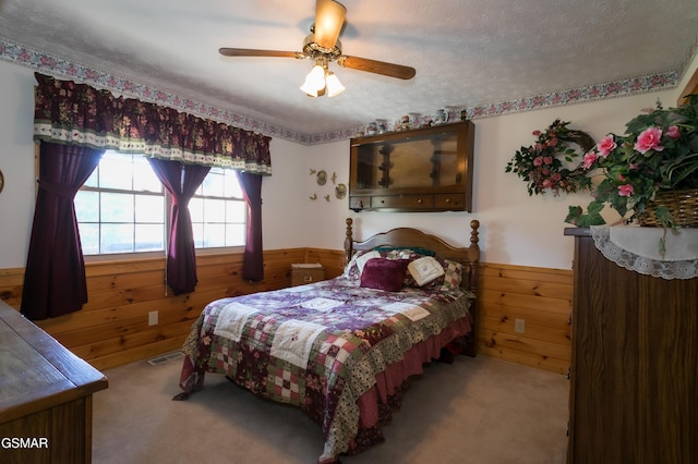 carpeted bedroom with ceiling fan, a textured ceiling, and wooden walls