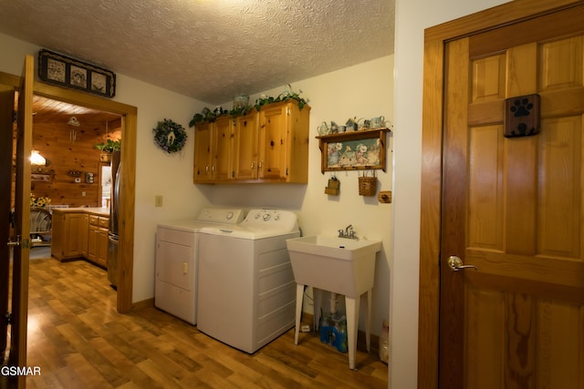 laundry room featuring cabinets, wooden walls, a textured ceiling, light hardwood / wood-style floors, and washing machine and clothes dryer