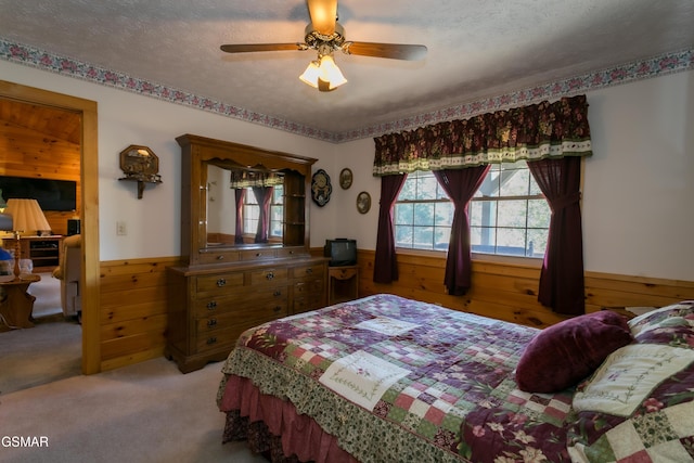 bedroom with carpet, a textured ceiling, ceiling fan, and wood walls