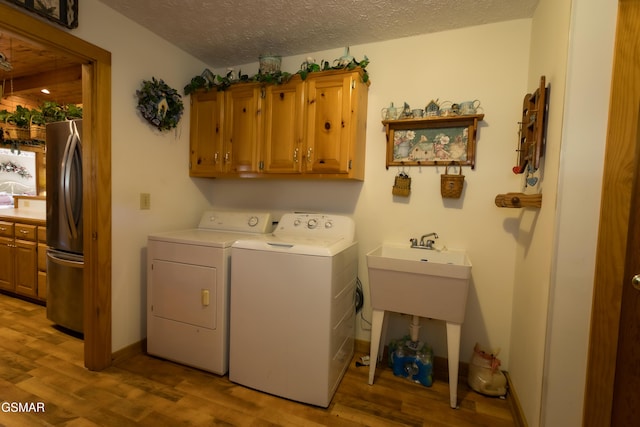 laundry room with cabinets, a textured ceiling, light wood-type flooring, and washing machine and clothes dryer