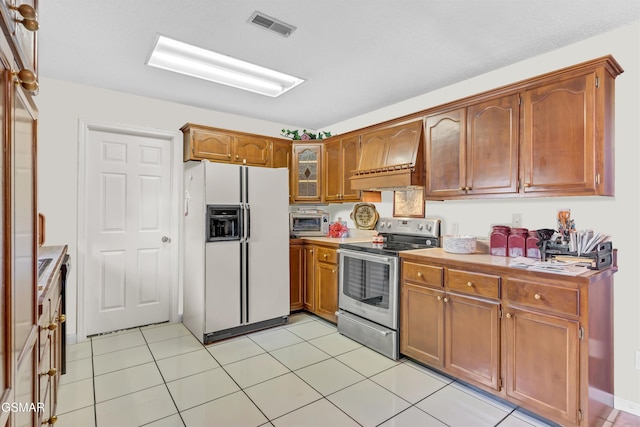 kitchen with light tile patterned floors, white refrigerator with ice dispenser, stainless steel range with electric cooktop, and premium range hood