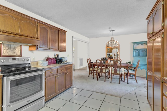 kitchen with stainless steel electric range oven, light tile patterned floors, hanging light fixtures, and an inviting chandelier