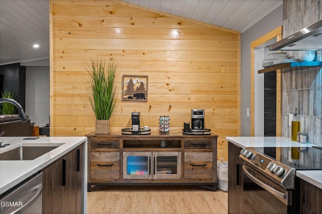 kitchen featuring light wood finished floors, stainless steel appliances, lofted ceiling, a sink, and wall chimney range hood