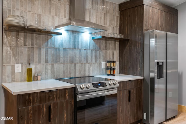 kitchen with wall chimney exhaust hood, appliances with stainless steel finishes, light countertops, and tile walls