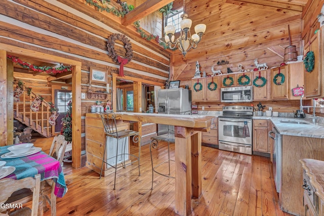 kitchen with sink, an inviting chandelier, decorative light fixtures, wooden walls, and appliances with stainless steel finishes