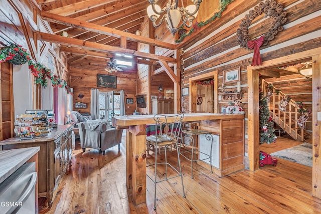 kitchen with ceiling fan with notable chandelier, light hardwood / wood-style flooring, high vaulted ceiling, and wood walls